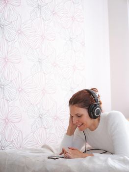 Vertical photo of a woman touching the screen of the mobile while listening to music in the bed