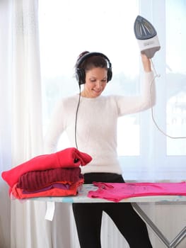 Vertical photo of a woman ironing while dancing at home next to a window with sunlight