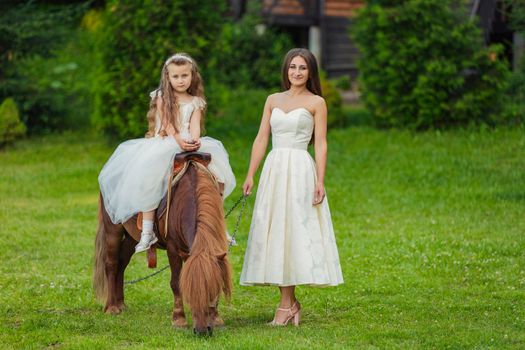 mother with daughter and pony walking in the yard