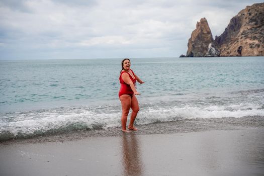 Woman in a bathing suit at the sea. A fat young woman in a red swimsuit enters the water during the surf.