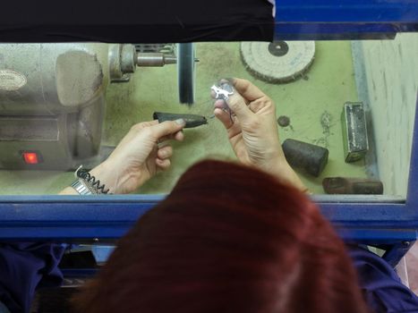 Top view of an unrecognizable adult woman working in a polishing machine with a safety box in her jewelry workshop.