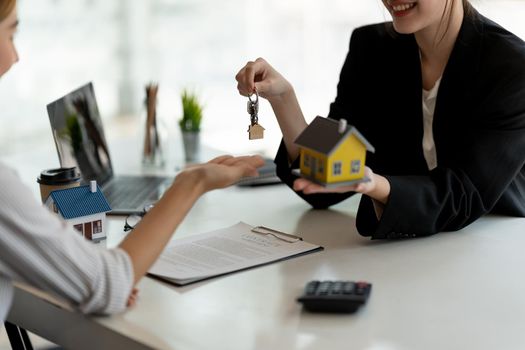 real estate agent holding house key to his client after signing contract agreement in office,concept for real estate, moving home or renting property.