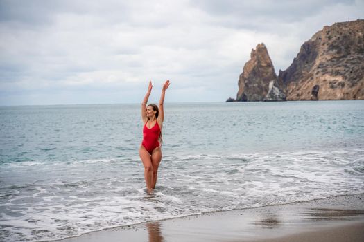 A beautiful and sexy brunette in a red swimsuit on a pebble beach, Running along the shore in the foam of the waves.