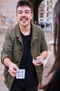 Vertical photo of a young street magician showing a card to the audience while performing a trick