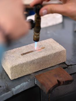 Vertical image of a woman working in her artisan jewelry workshop using a torch to perform her work on a block of stone