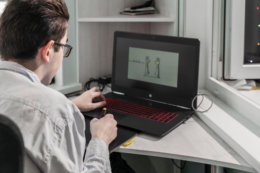 Young male student 3D designer uses graphics tablet to work at the table