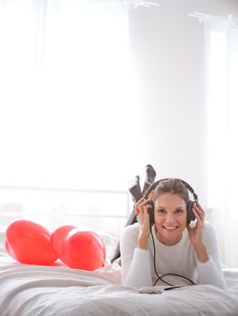 Vertical photo with copy space of a smiling woman listening to music in bed with the mobile