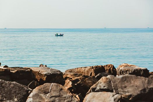 fishermen at work in the Ligurian coast of Imperia, a view with rocks, sea and horizon with ships in the background