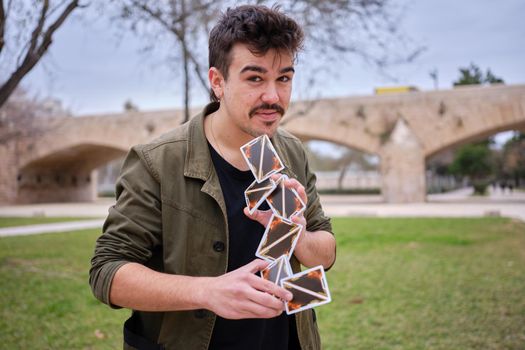 Magician making a card castle while looking at the cacmera and performing a trick in a park