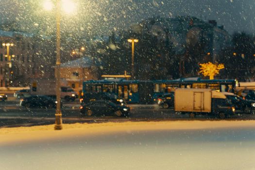 Winter blurred background with falling snow on the background of road traffic on a city street