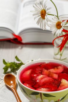 Cherry jelly with strawberry pieces in the bowl with opened book and chamomiles on the background