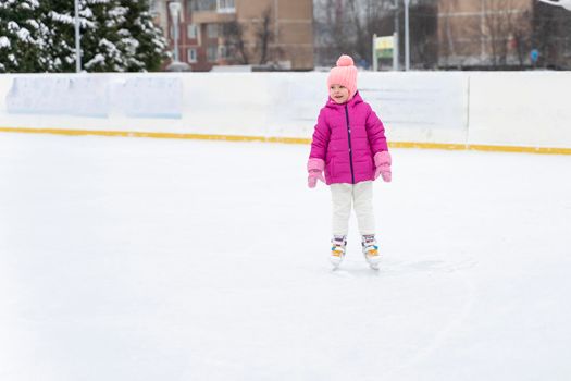 little girl in a red jacket is skating on the ice rink