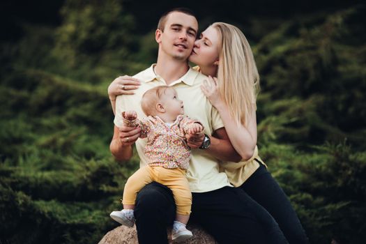 happy husband and wife with their lovely child. Handsome man holding little baby and beautiful woman hugging him from back. Young family in casual clothes walking together in sunny day.