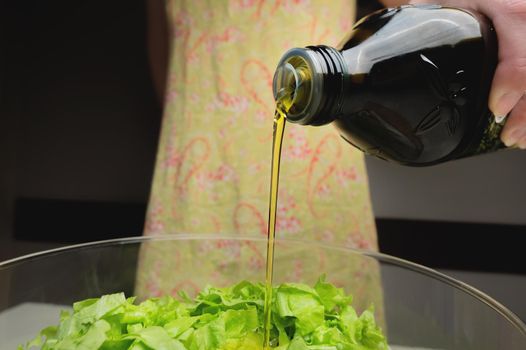 close-up of young woman dressing vegetable salad in glass bowl, olive oil at home. vegetarian dish