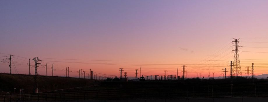 Panoramic photo of a vivid sunset with silhouettes of electric towers on the background