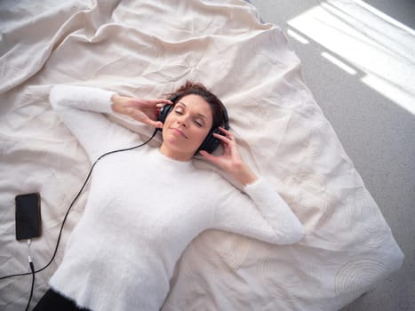 Top view of a woman relaxed lying on the bed with eyes closed and listening to music with the mobile