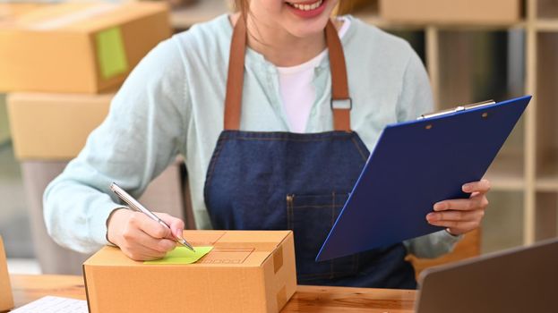 Small business entrepreneur working at home office, writing address on cardboard box.