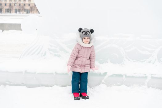 little girl in a knitted hat and scarf and ice sculptures