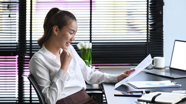 Happy young female employee reading good news on digital tablet and celebrating business success.