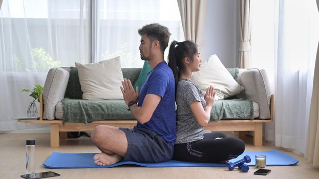 Calm young couple meditating, in lotus position at home. Healthy lifestyle, yoga, pilates, exercising concept.