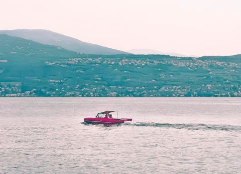 red amphibious car floats in the lake of a small town in France