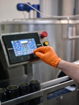 Vertical photo of the hand with gloves of a man working with an electronic machine in a brewery