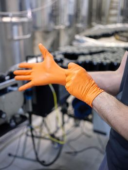 Vertical photo of the hand of a worker putting on latex gloves in a canning beer factory