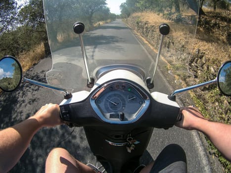 person riding a scooter on a country road, you see your hands holding the handlebars.