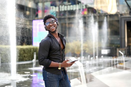 Portrait of an african man smiling while listening to music with the mobile ouside a shopping mall