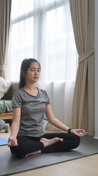 Peaceful young woman sitting on lotus position on floor with eyes closed. Healthy lifestyle concept.