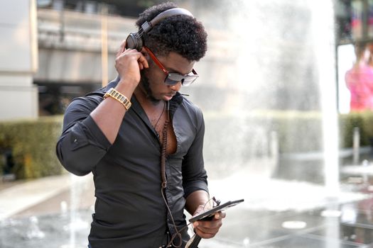 African man adjusting his headphones while listening to music on his mobile phone.