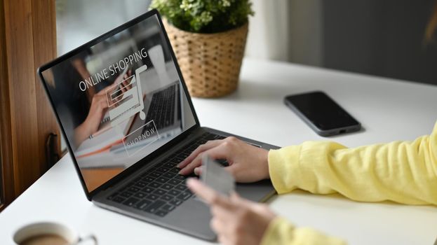 Cropped shot young woman holding credit card and using internet banking service on her computer laptop.