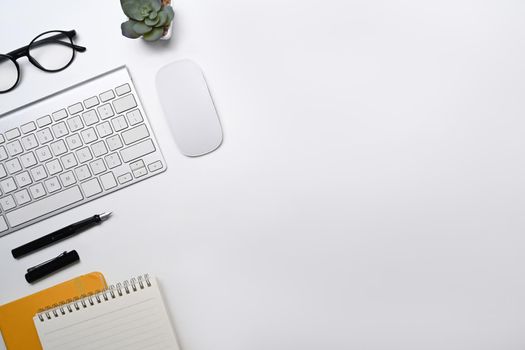 Top view white office desk with wireless keyboard, glasses, notebook and succulent plant.