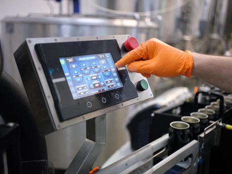 Hand of a worker with a glove touching the screen of an electronic machine ina canning factory