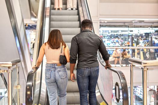 African man and asian woman of walking up an escalator in a shopping mall in Bangkok, Thailand