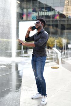 Vertical photo of a black man doing a stop gesture while talking to the mobile outside a mall