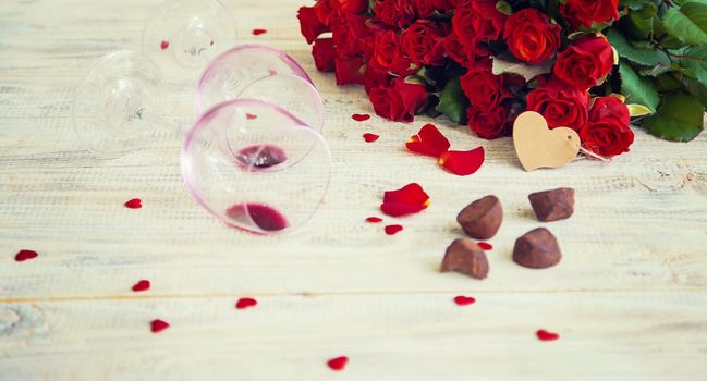 A bouquet of red roses and red wine in glasses. Valentine's Day. Selective focus. Holiday.