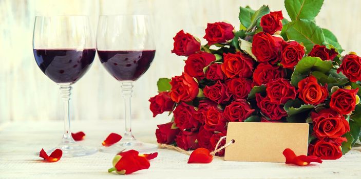 A bouquet of red roses and red wine in glasses. Valentine's Day. Selective focus. Holiday.