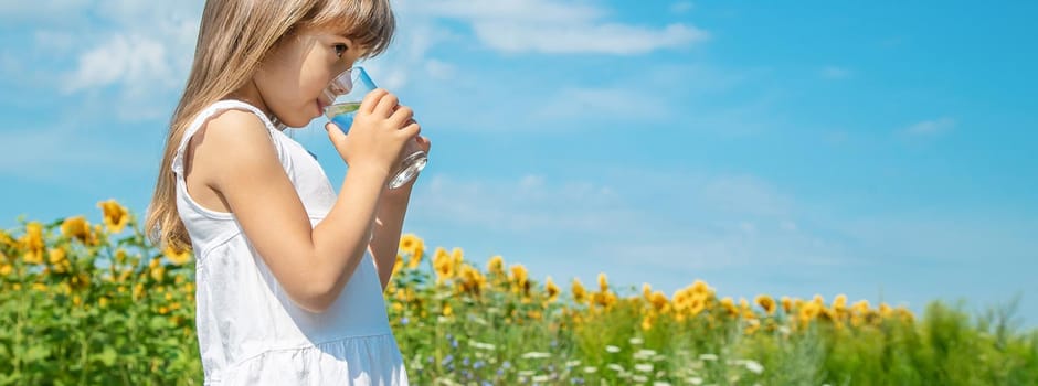 A child drinks water on the background of the field. Selective focus.