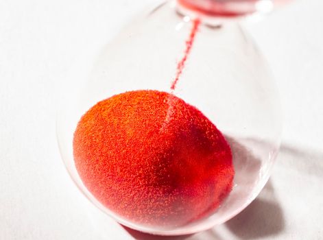 hourglass with red sand used to measure time flow, macro photography