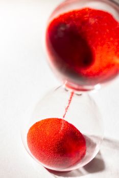 hourglass with red sand used to measure time flow, macro photography