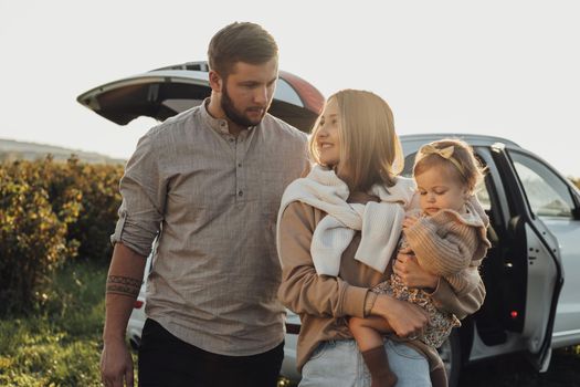 Young Caucasian Family Enjoying Road Trip, Mother and Father with Little Daughter Outdoors with SUV Car on Background