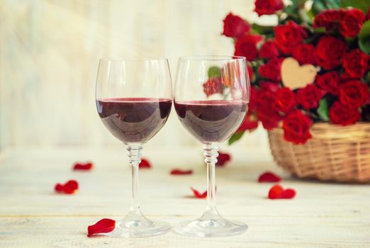 A bouquet of red roses and red wine in glasses. Valentine's Day. Selective focus. Holiday.