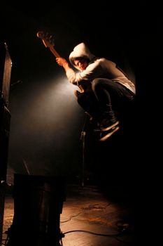 A young musician jumps on stage with his guitar during a live concert.
