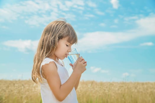 A child drinks water on the background of the field. Selective focus.