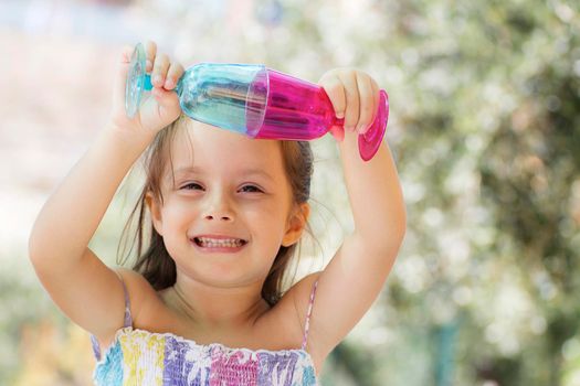 A smiling little girl play with colored glasses.