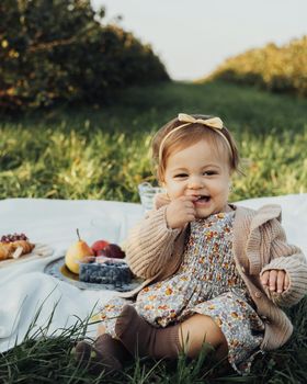 Vertical Portrait of Cheerful Little Baby Girl Sitting on Plaid on Picnic Outdoors at Sunset