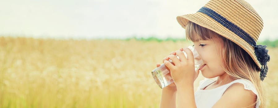 A child drinks water on the background of the field. Selective focus.