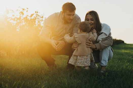 Portrait of Happy Young Caucasian Family, Mother and Father with Baby Daughter Outdoors at Sunset