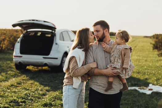 Young Caucasian Family Enjoying Road Trip, Mother and Father with Little Daughter Outdoors with SUV Car on Background